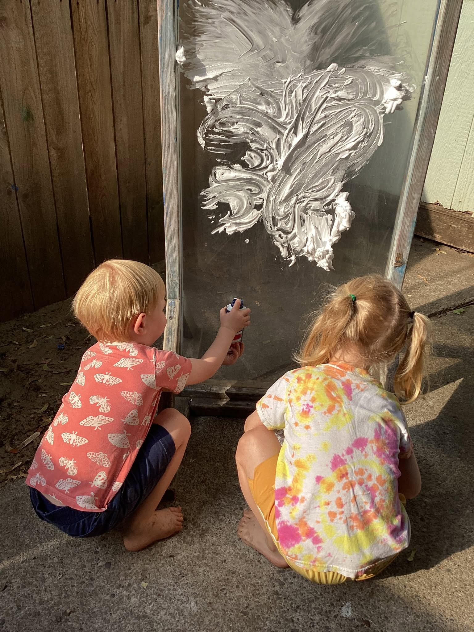 Two children exploring shaving cream art on an outdoor easel at In A Child's Path
